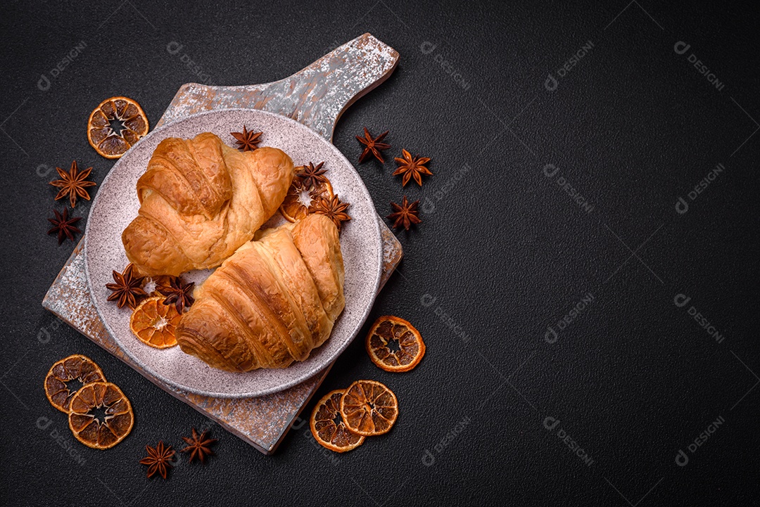 Deliciosos croissants doces assados ​​e crocantes com recheio em uma placa de cerâmica sobre um fundo escuro de concreto