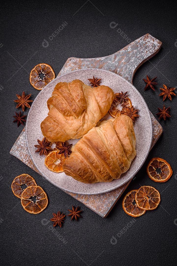 Deliciosos croissants doces assados ​​e crocantes com recheio em uma placa de cerâmica sobre um fundo escuro de concreto