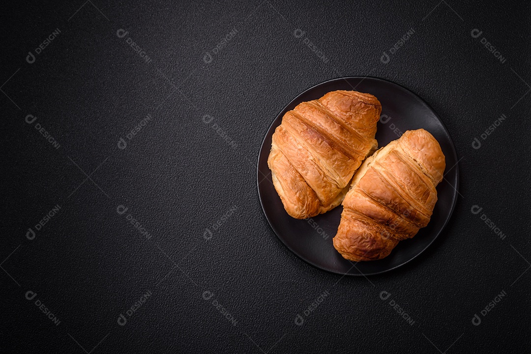 Deliciosos croissants doces assados ​​e crocantes com recheio em uma placa de cerâmica sobre um fundo escuro de concreto