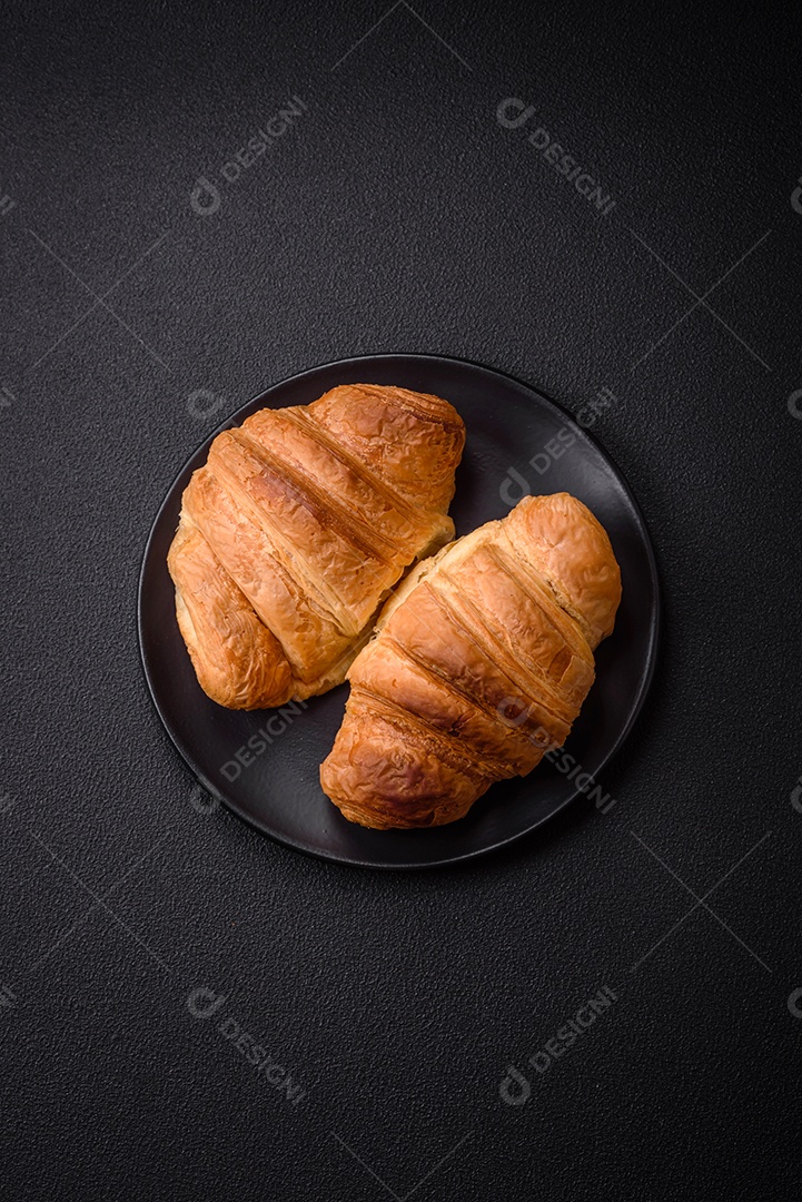 Deliciosos croissants doces assados ​​e crocantes com recheio em uma placa de cerâmica sobre um fundo escuro de concreto