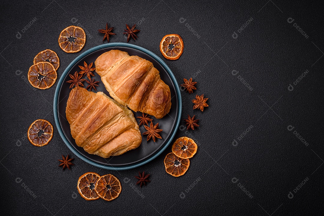 Deliciosos croissants doces assados ​​e crocantes com recheio em uma placa de cerâmica sobre um fundo escuro de concreto