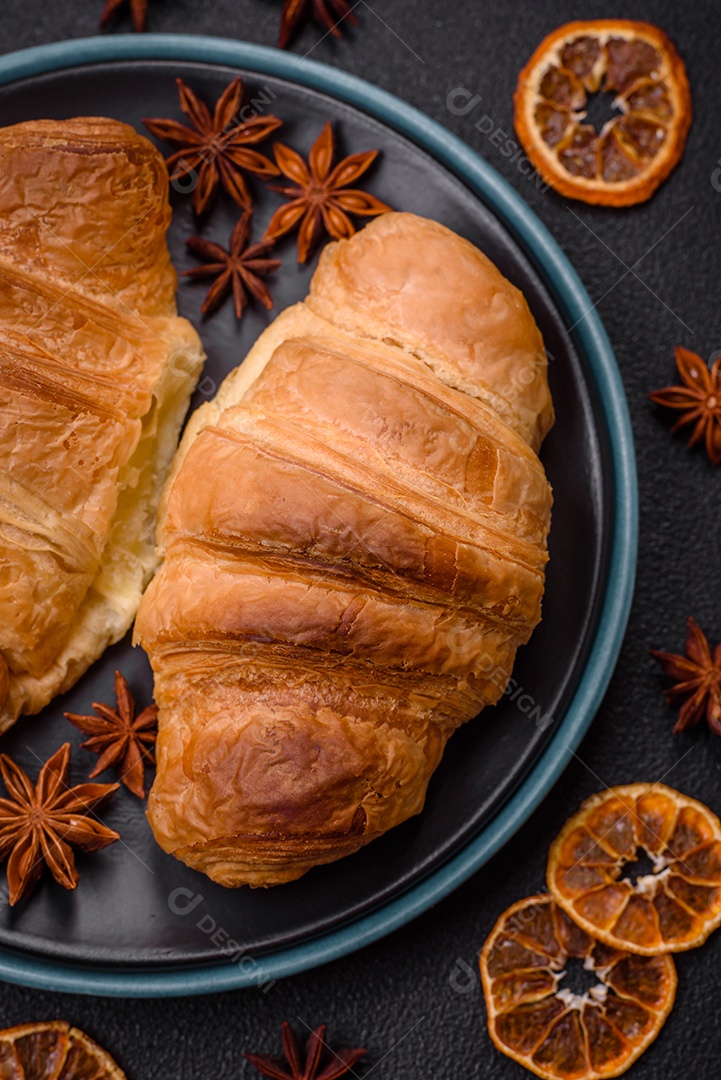 Deliciosos croissants doces assados ​​e crocantes com recheio em uma placa de cerâmica sobre um fundo escuro de concreto
