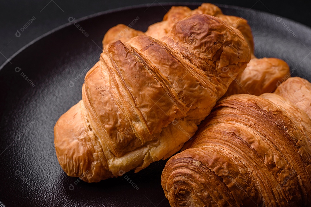 Deliciosos croissants doces assados ​​e crocantes com recheio em uma placa de cerâmica sobre um fundo escuro de concreto