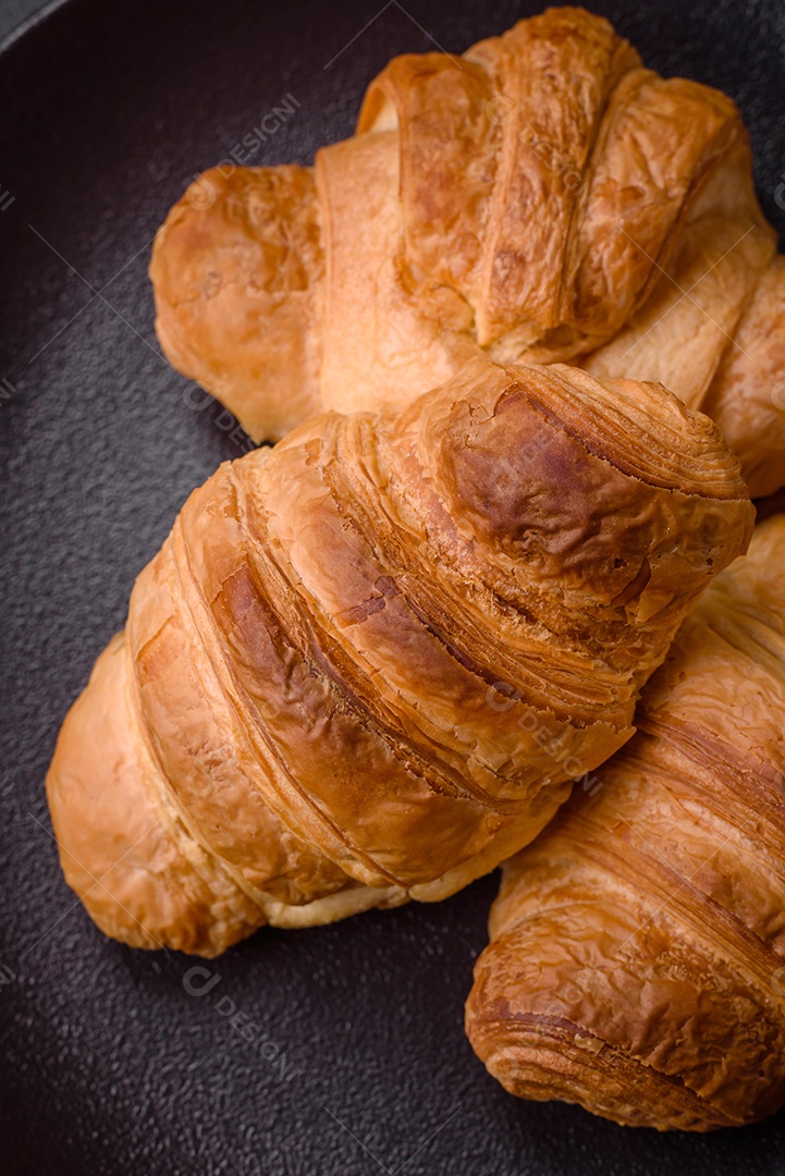Deliciosos croissants doces assados ​​e crocantes com recheio em uma placa de cerâmica sobre um fundo escuro de concreto