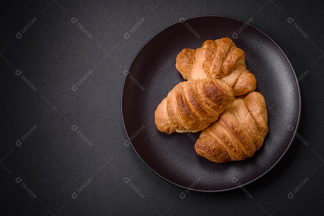 Deliciosos croissants doces assados ​​e crocantes com recheio em uma placa de cerâmica sobre um fundo escuro de concreto