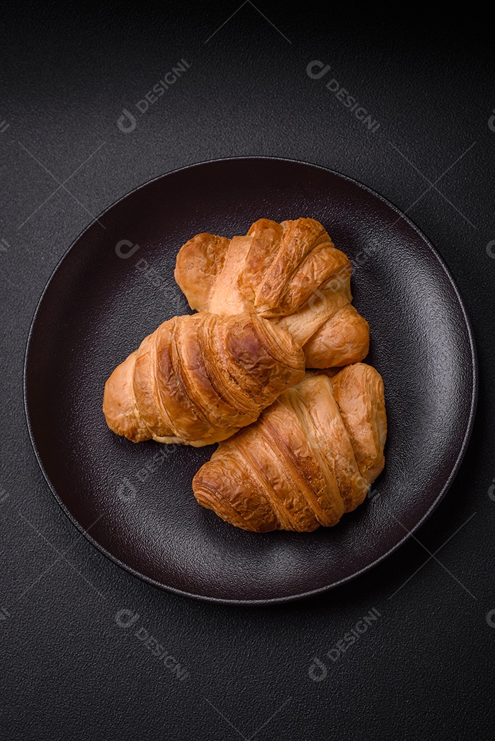 Deliciosos croissants doces assados ​​e crocantes com recheio em uma placa de cerâmica sobre um fundo escuro de concreto