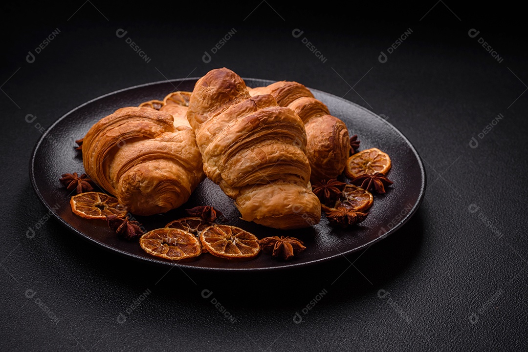 Deliciosos croissants doces assados ​​e crocantes com recheio em uma placa de cerâmica sobre um fundo escuro de concreto