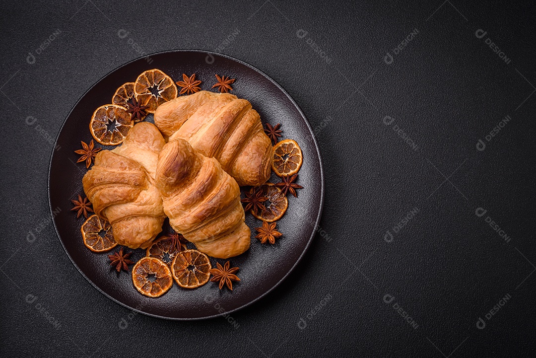 Deliciosos croissants doces assados ​​e crocantes com recheio em uma placa de cerâmica sobre um fundo escuro de concreto