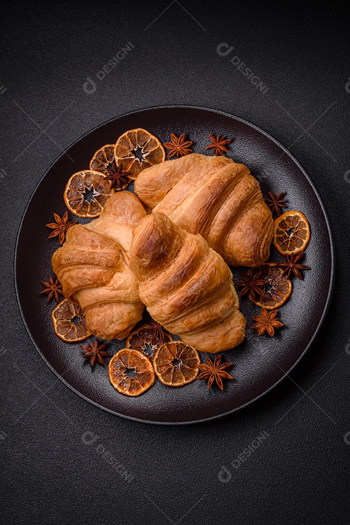 Deliciosos croissants doces assados ​​e crocantes com recheio em uma placa de cerâmica sobre um fundo escuro de concreto