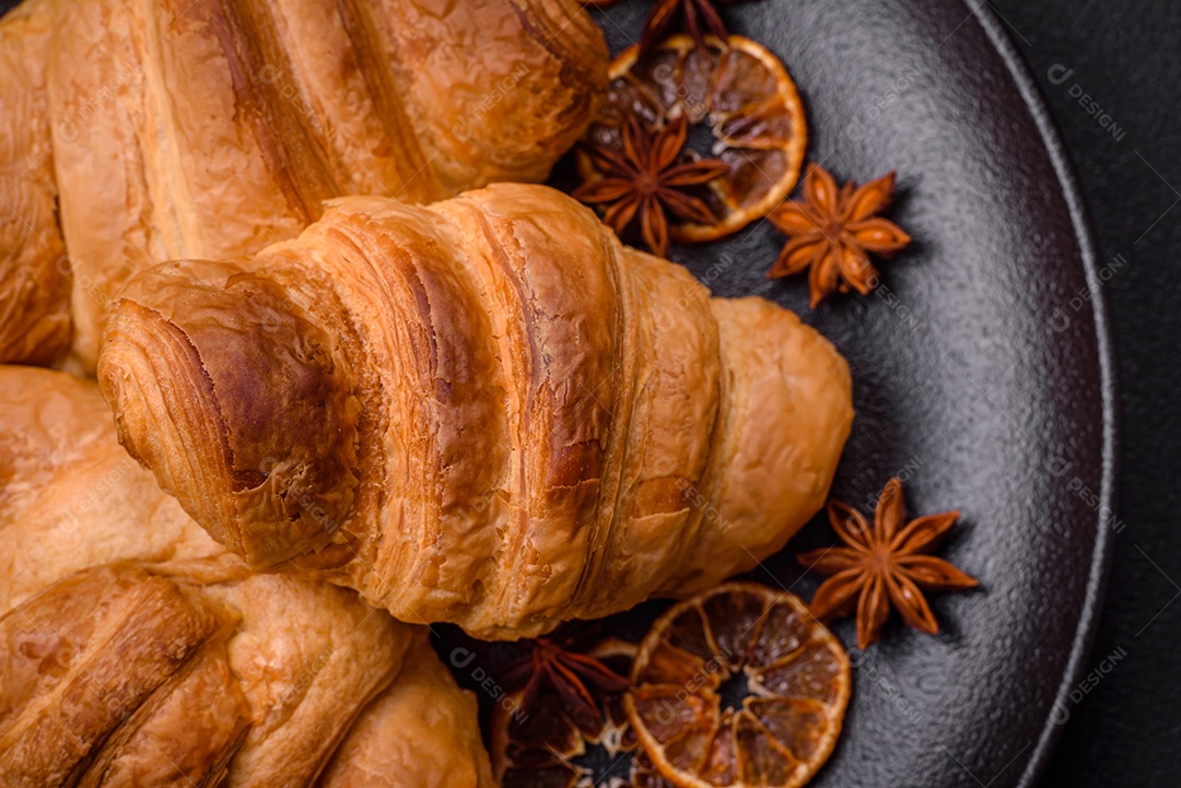 Deliciosos croissants doces assados ​​e crocantes com recheio em uma placa de cerâmica sobre um fundo escuro de concreto