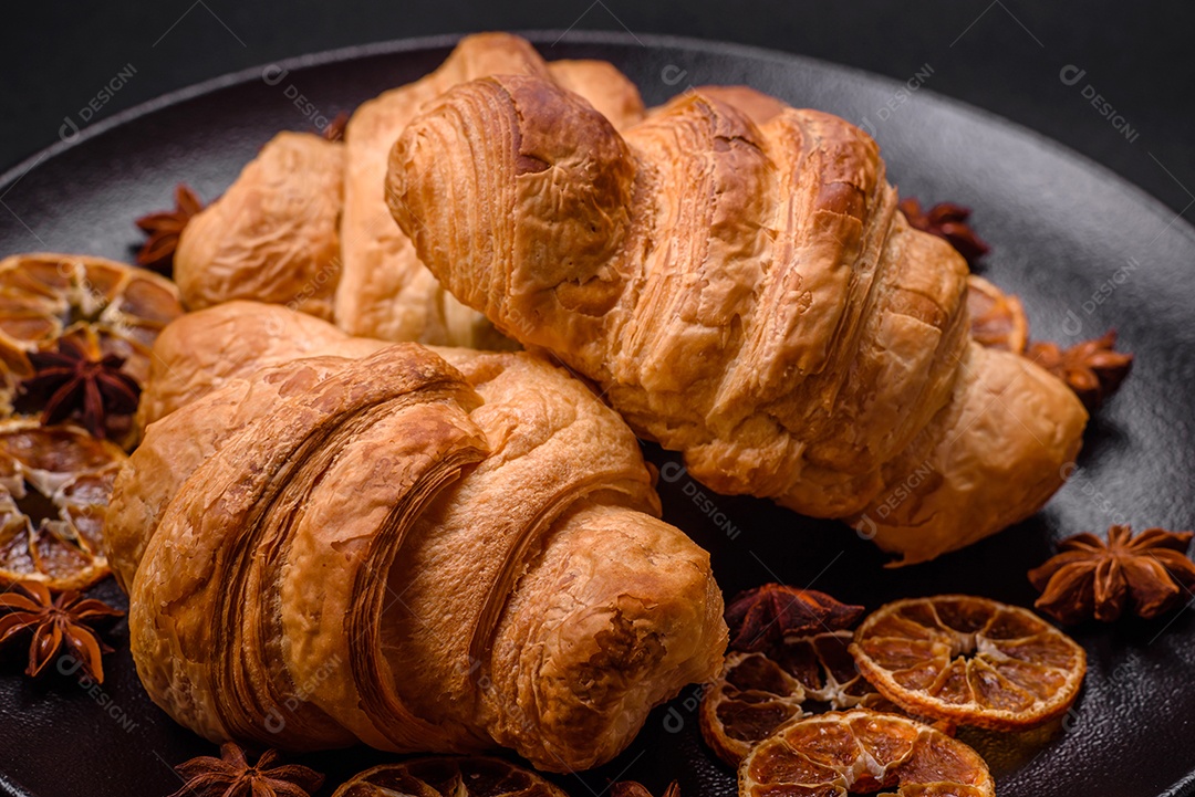 Deliciosos croissants doces assados ​​e crocantes com recheio em uma placa de cerâmica sobre um fundo escuro de concreto