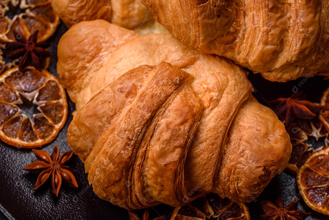 Deliciosos croissants doces assados ​​e crocantes com recheio em uma placa de cerâmica sobre um fundo escuro de concreto