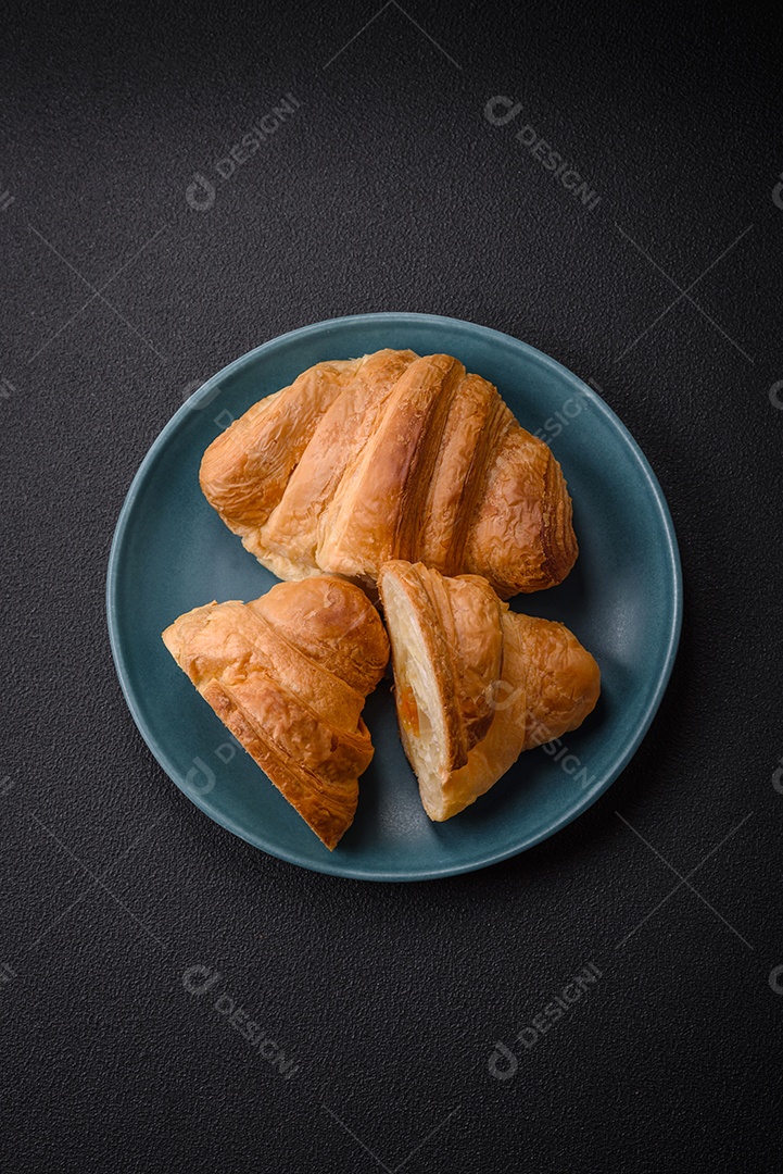 Deliciosos croissants doces assados ​​e crocantes com recheio em uma placa de cerâmica sobre um fundo escuro de concreto