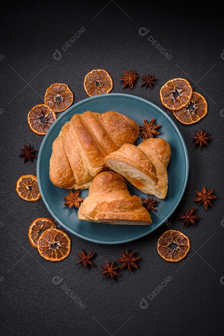 Deliciosos croissants doces assados ​​e crocantes com recheio em uma placa de cerâmica sobre um fundo escuro de concreto