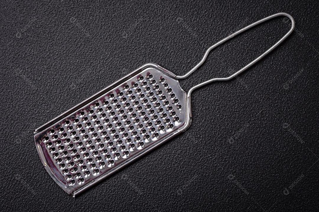 Lindo ralador de cozinha de metal pequeno com alça em um fundo escuro e texturizado