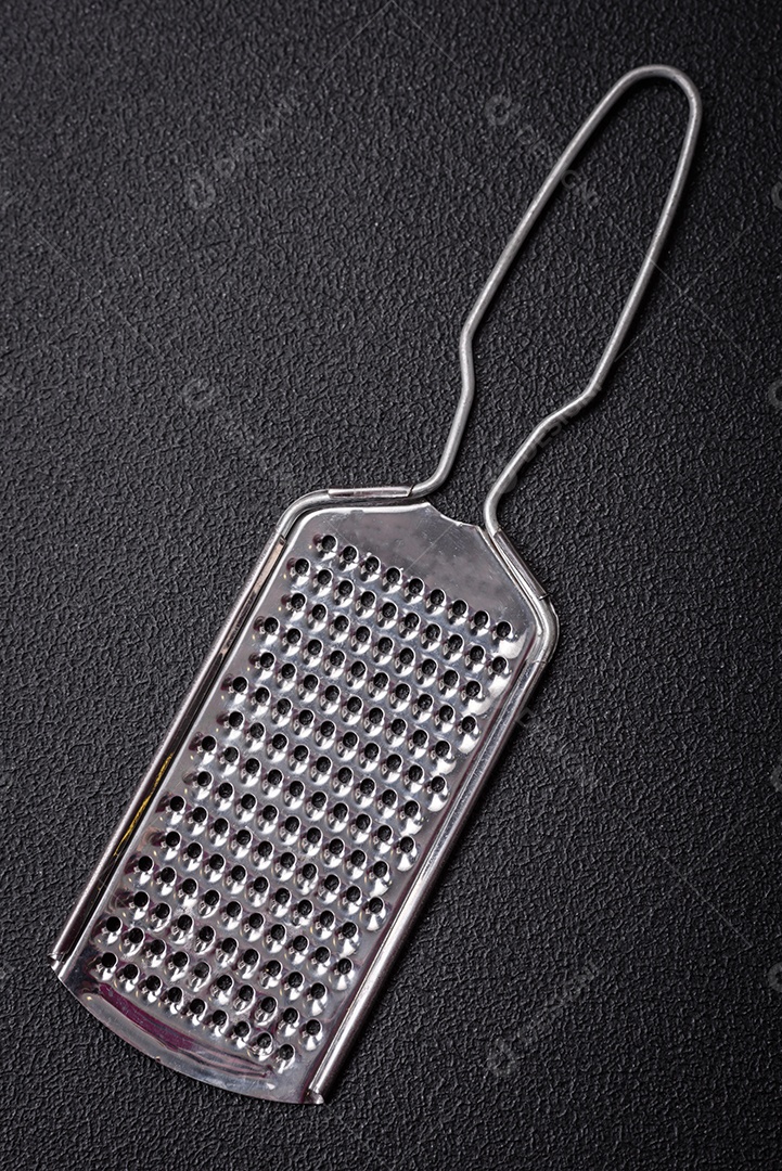 Lindo ralador de cozinha de metal pequeno com alça em um fundo escuro e texturizado