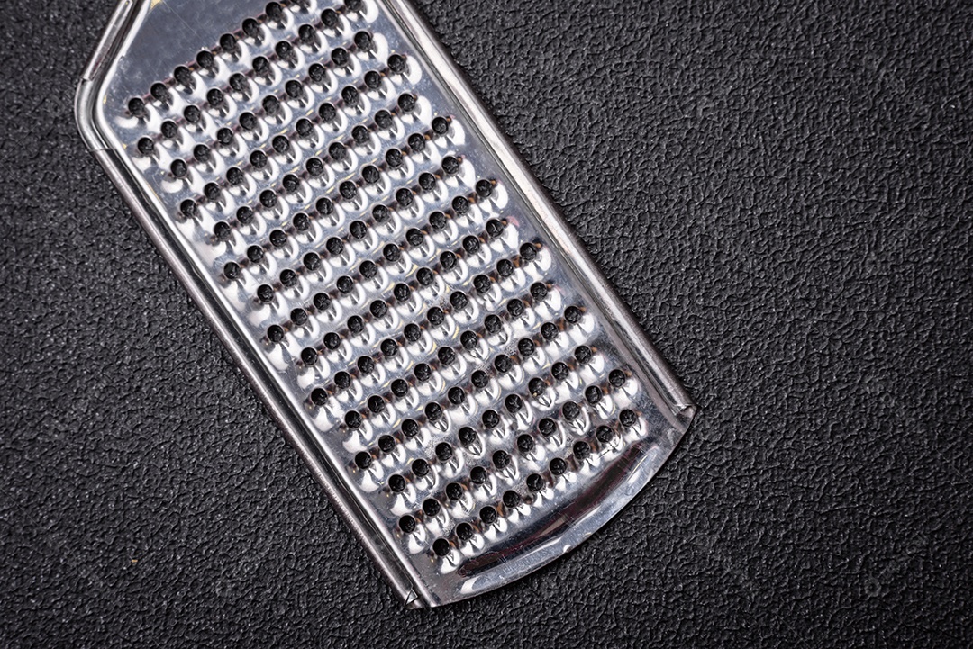 Lindo ralador de cozinha de metal pequeno com alça em um fundo escuro e texturizado