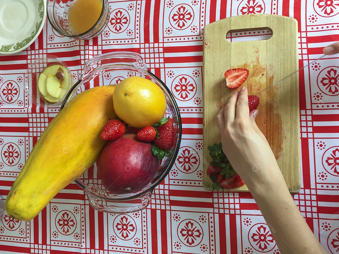 Mãos femininas cortando morango em pequenas fatias