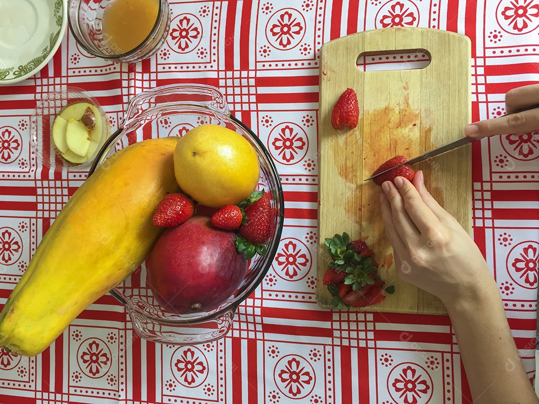 Mãos femininas cortando morango em pequenas fatias