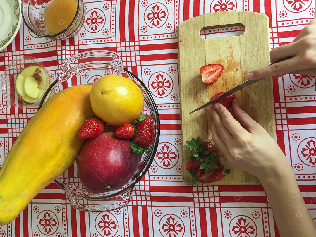 Mãos femininas cortando morango em pequenas fatias