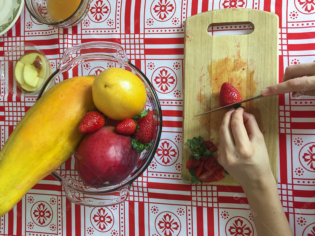 Mãos femininas cortando morango em pequenas fatias
