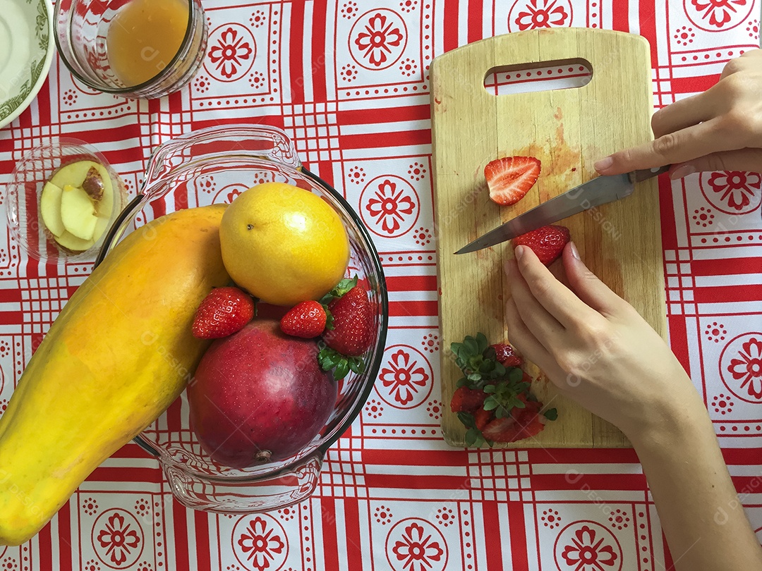 Mãos femininas cortando morango em pequenas fatias