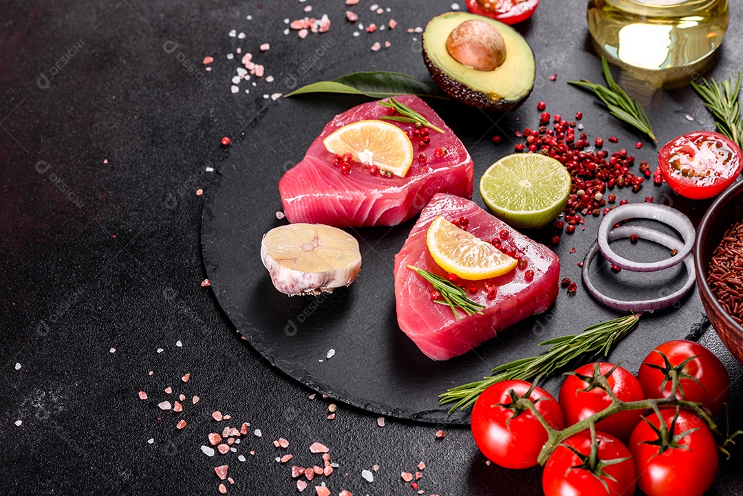 Bifes de filé de atum fresco com especiarias e ervas sobre fundo preto.