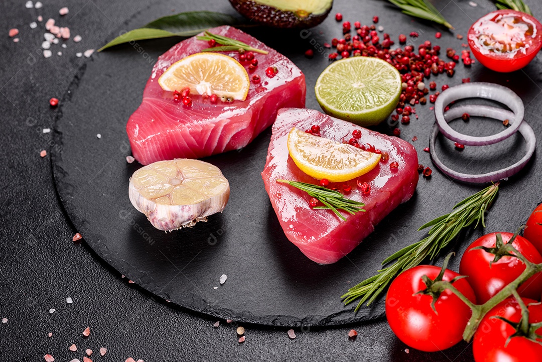 Bifes de filé de atum fresco com especiarias e ervas sobre fundo preto.