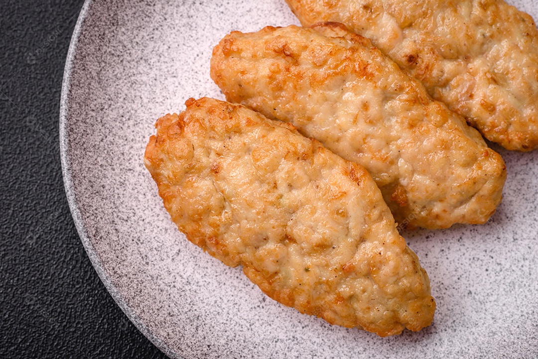 Deliciosos peixes picados fritos frescos ou costeletas de frango com especiarias e ervas sobre um fundo escuro de concreto