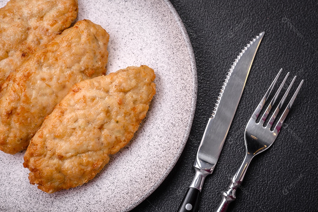 Deliciosos peixes picados fritos frescos ou costeletas de frango com especiarias e ervas sobre um fundo escuro de concreto
