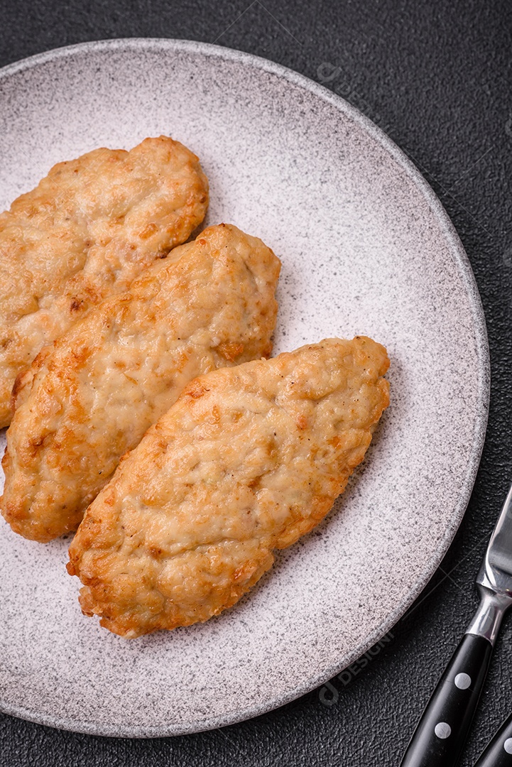 Deliciosos peixes picados fritos frescos ou costeletas de frango com especiarias e ervas sobre um fundo escuro de concreto