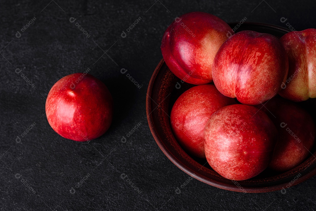 Deliciosos pêssegos ou nectarinas doces em uma tigela marrom sobre um fundo escuro de concreto