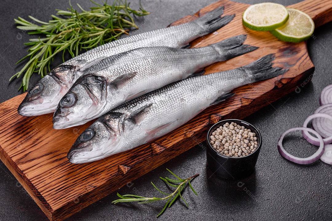Robalo de peixe fresco e ingredientes para cozinhar. Robalo de peixe cru com especiarias e ervas em uma mesa escura