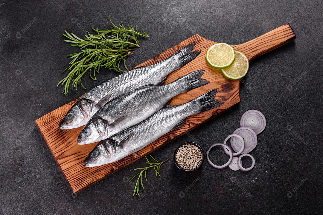 Robalo de peixe fresco e ingredientes para cozinhar. Robalo de peixe cru com especiarias e ervas em uma mesa escura