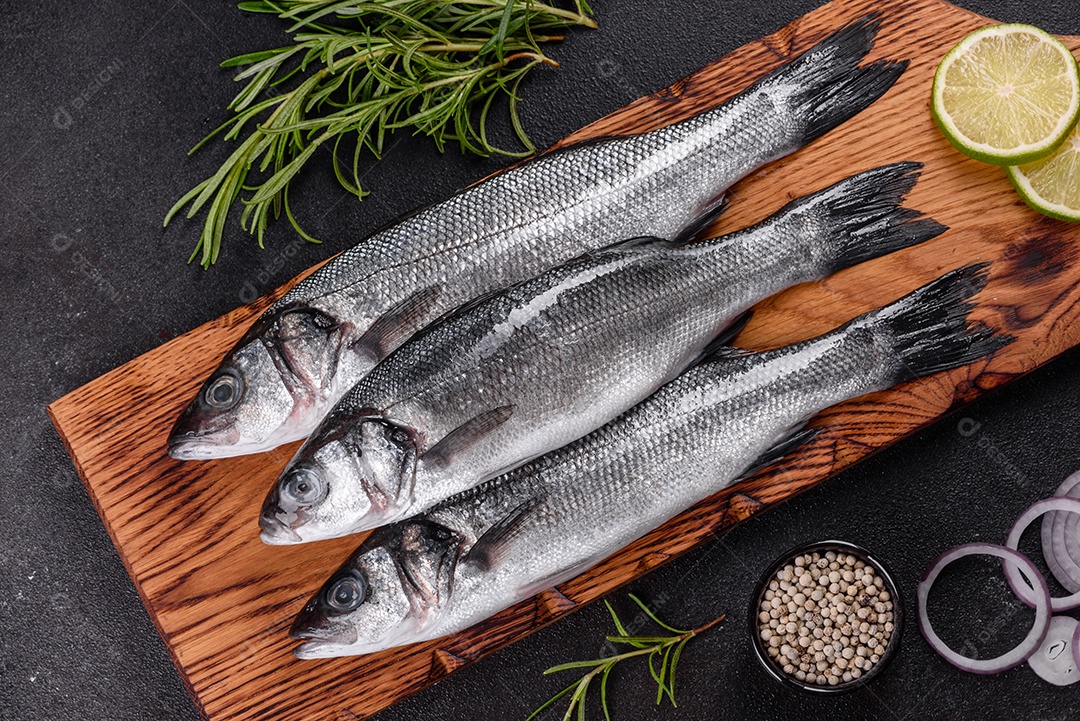 Robalo de peixe fresco e ingredientes para cozinhar. Robalo de peixe cru com especiarias e ervas em uma mesa escura