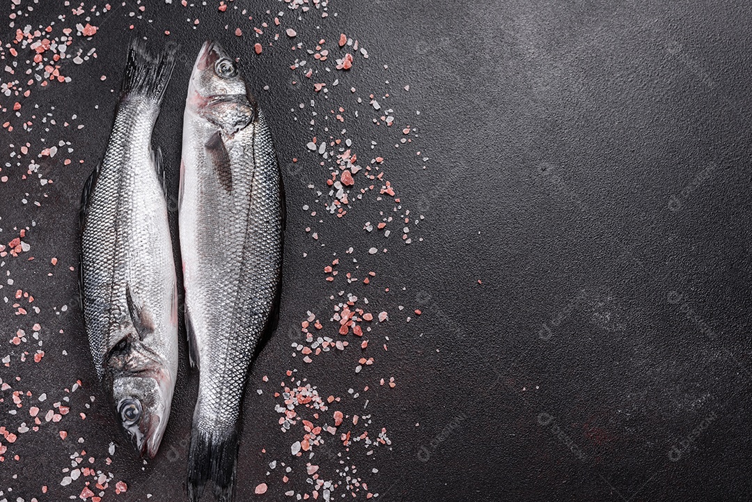 Robalo de peixe fresco e ingredientes para cozinhar. Robalo de peixe cru com especiarias e ervas em uma mesa escura