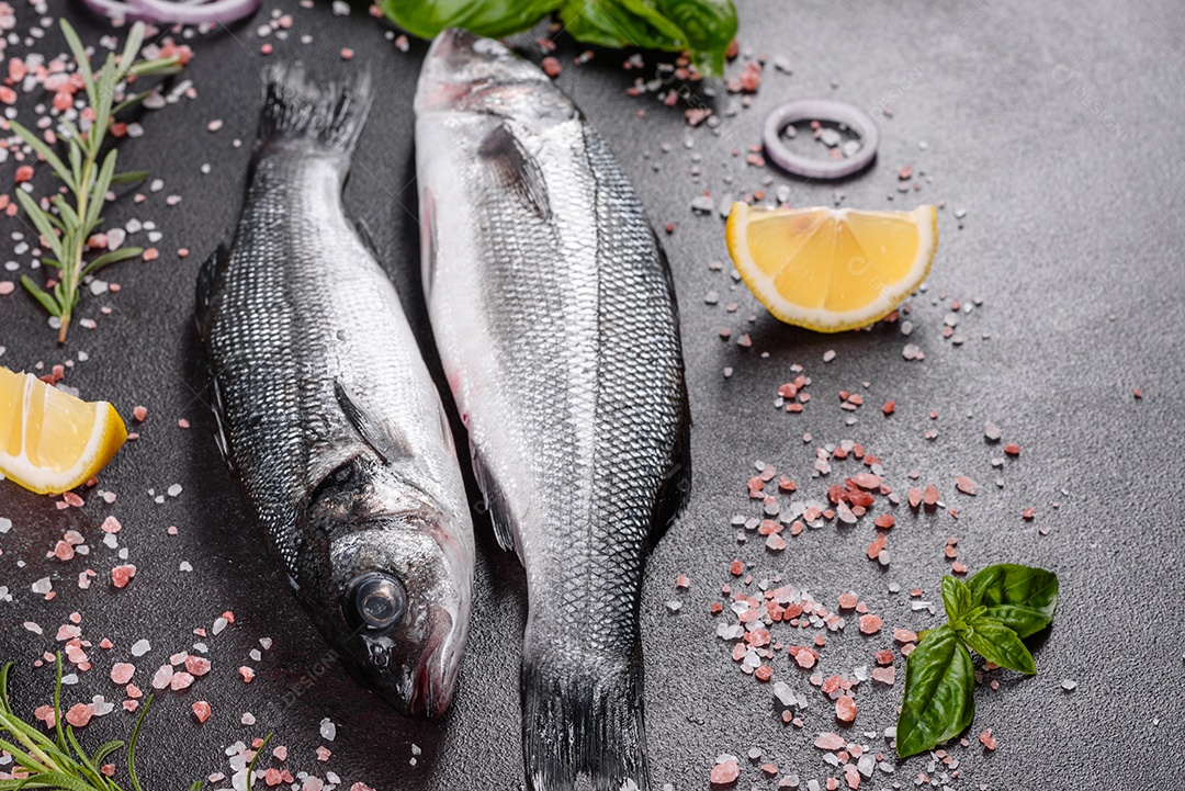 Robalo de peixe fresco e ingredientes para cozinhar. Robalo de peixe cru com especiarias e ervas em uma mesa escura