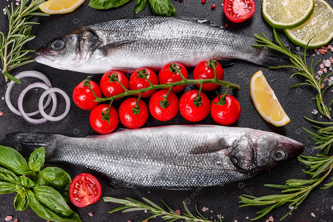 Robalo de peixe fresco e ingredientes para cozinhar. Robalo de peixe cru com especiarias e ervas em uma mesa escura