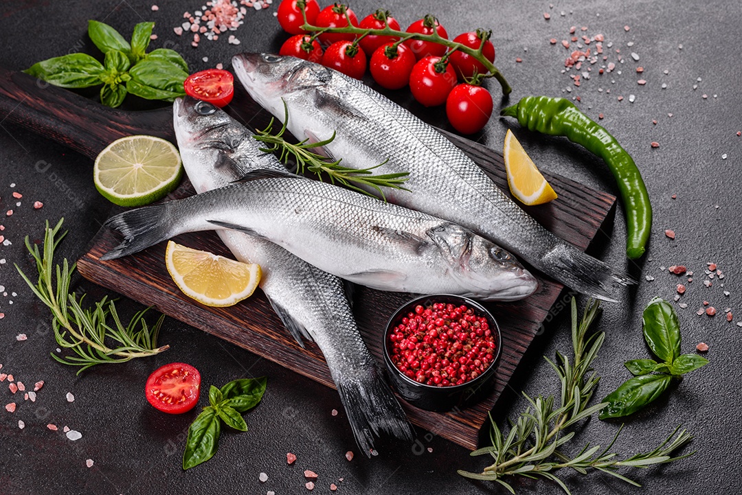 Robalo de peixe fresco e ingredientes para cozinhar. Robalo de peixe cru com especiarias e ervas em uma mesa escura