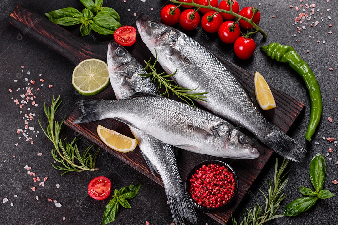 Robalo de peixe fresco e ingredientes para cozinhar. Robalo de peixe cru com especiarias e ervas em uma mesa escura
