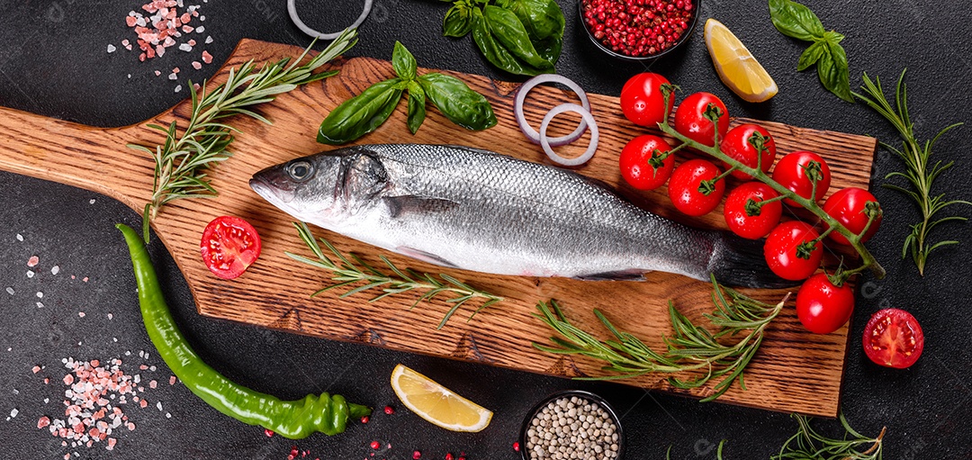 Robalo de peixe fresco e ingredientes para cozinhar. Robalo de peixe cru com especiarias e ervas em uma mesa escura