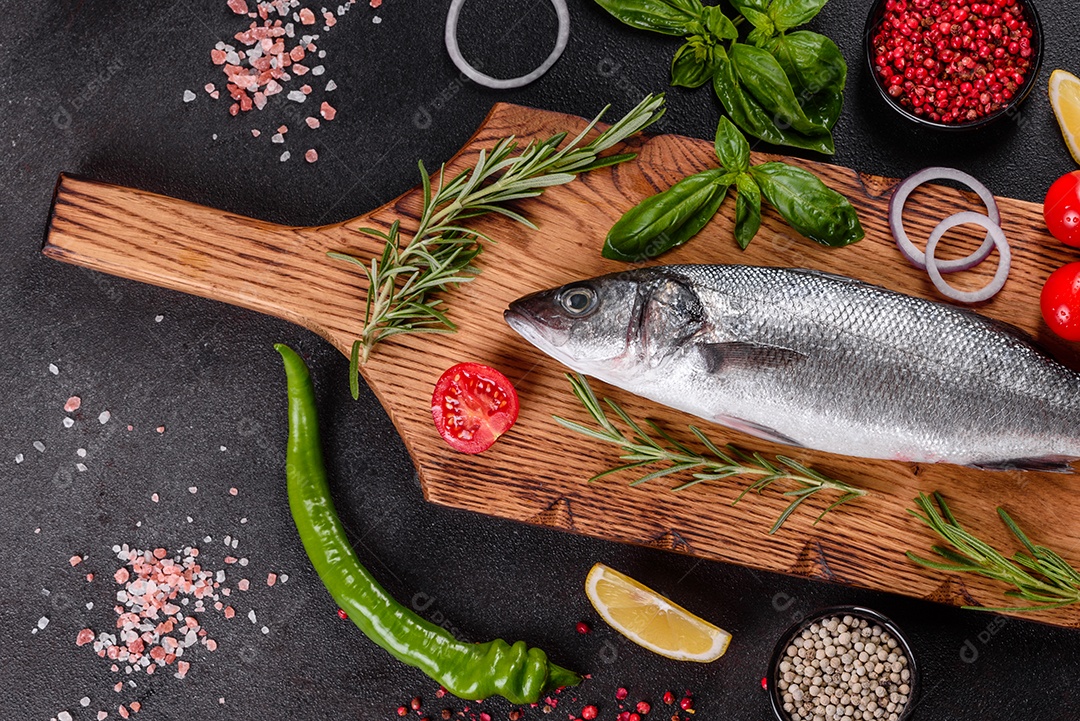 Robalo de peixe fresco e ingredientes para cozinhar. Robalo de peixe cru com especiarias e ervas em uma mesa escura