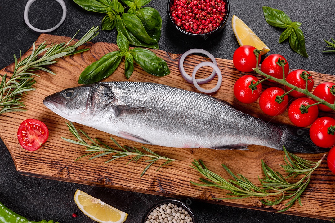 Robalo de peixe fresco e ingredientes para cozinhar. Robalo de peixe cru com especiarias e ervas em uma mesa escura