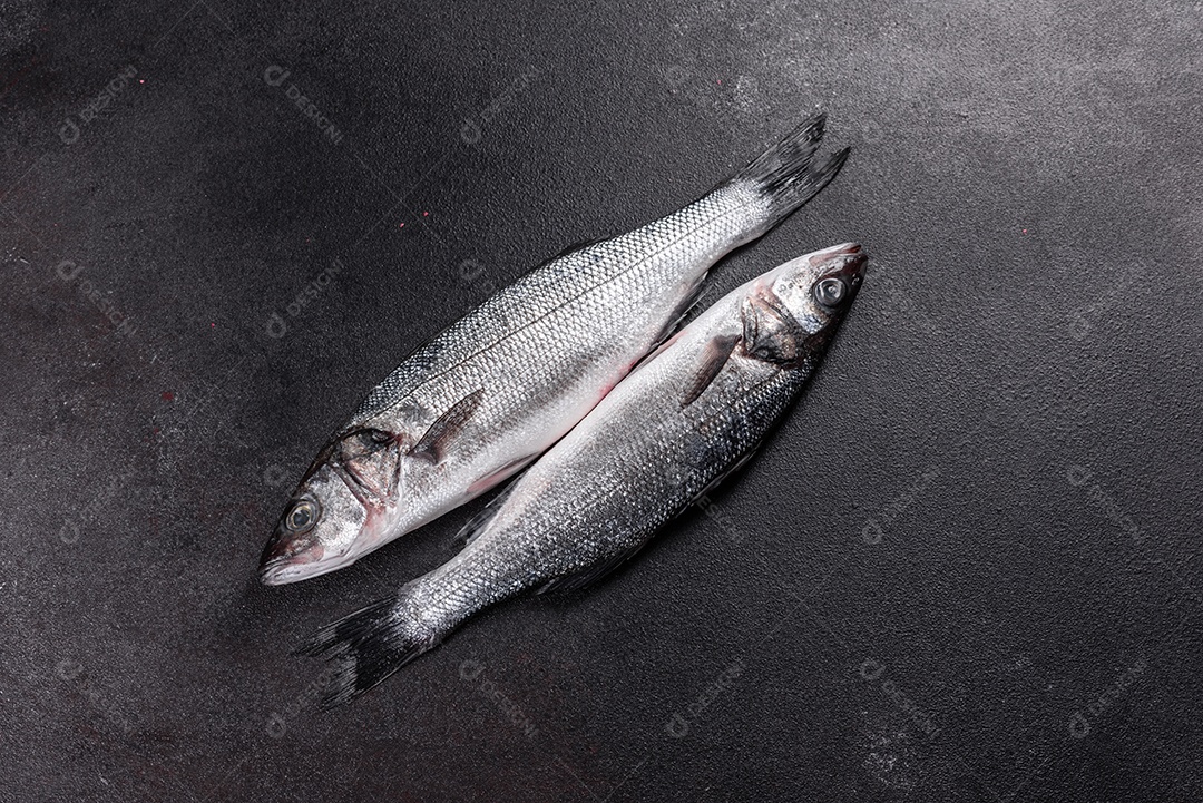 Robalo de peixe fresco e ingredientes para cozinhar. Robalo de peixe cru com especiarias e ervas em uma mesa escura