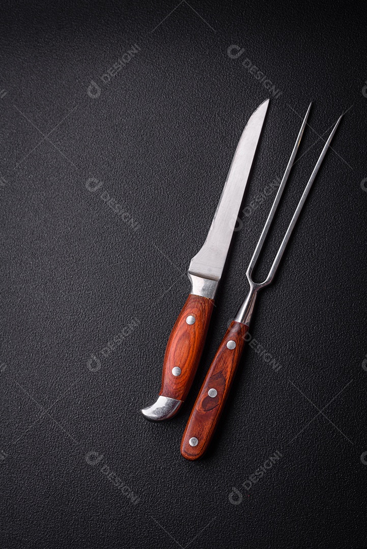 Faca e garfo de cozinha feitos de aço em um fundo escuro de concreto