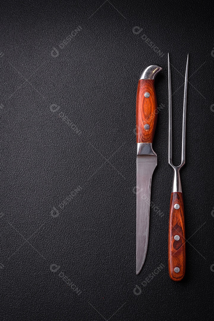 Faca e garfo de cozinha feitos de aço em um fundo escuro de concreto