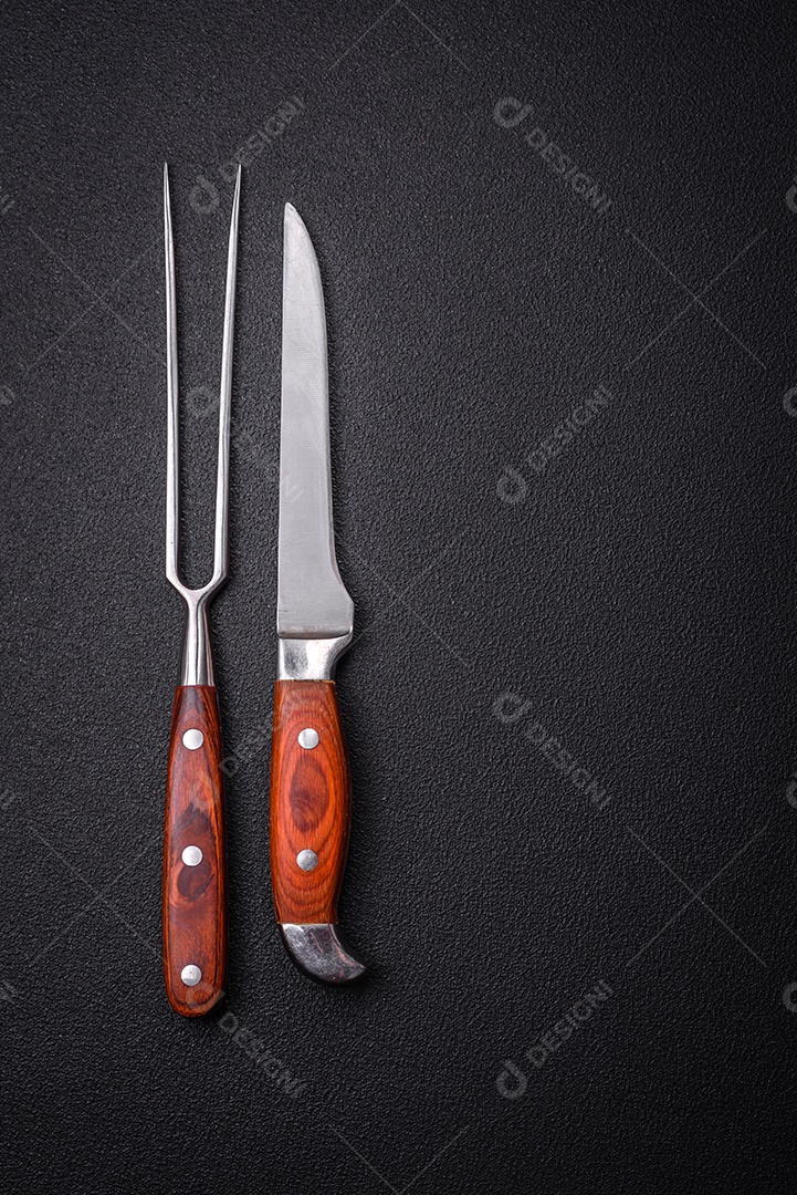 Faca e garfo de cozinha feitos de aço em um fundo escuro de concreto