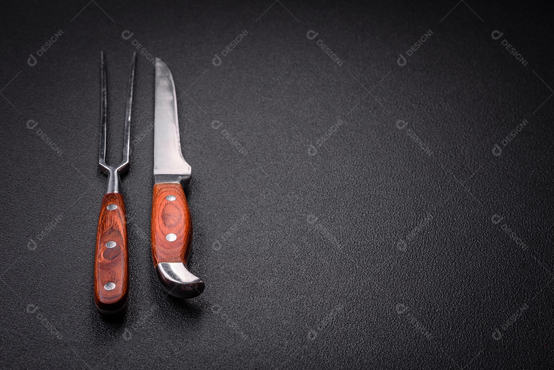 Faca e garfo de cozinha feitos de aço em um fundo escuro de concreto