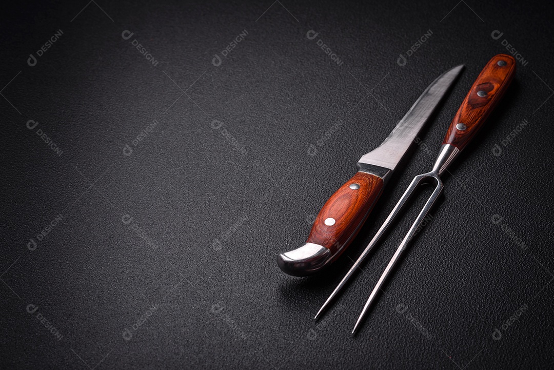 Faca e garfo de cozinha feitos de aço em um fundo escuro de concreto