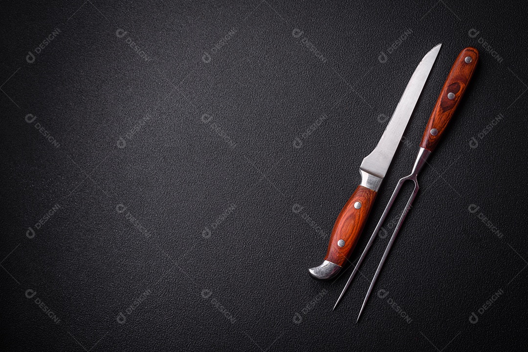 Faca e garfo de cozinha feitos de aço em um fundo escuro de concreto